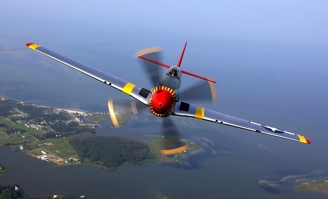 P-51 Mustang warbird in flight, polished aluminum fuselage catching the light