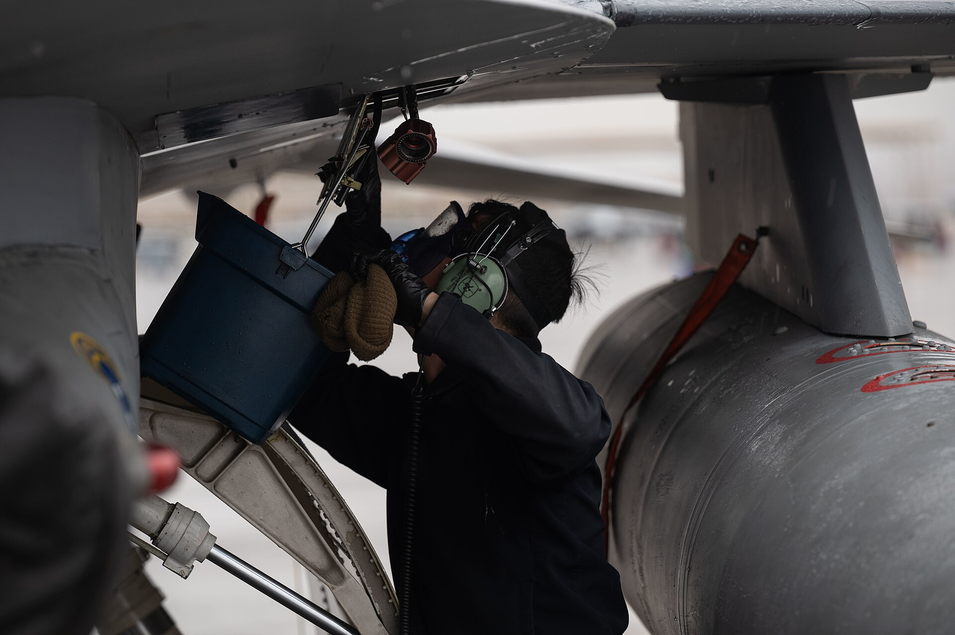Ground crew member wearing ear protection working under an aircraft wing on the flight line