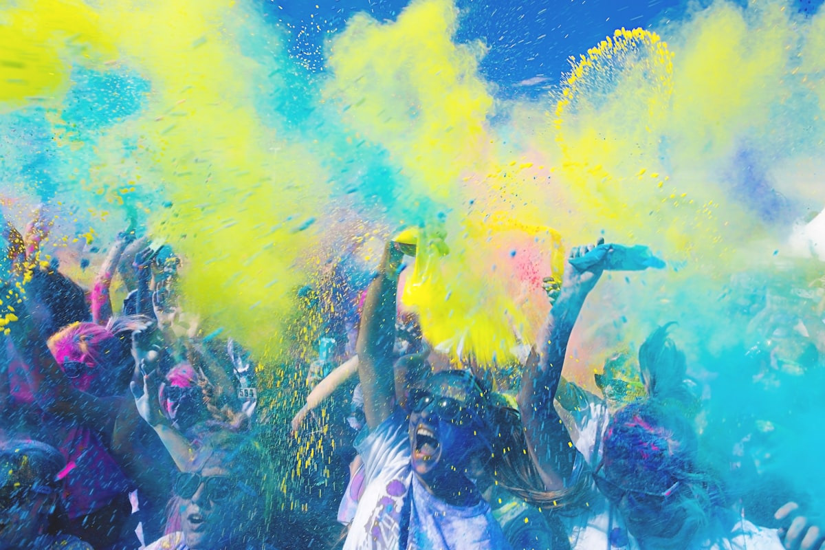 Fun-run participants celebrating in a cloud of bright color powder under a blue sky